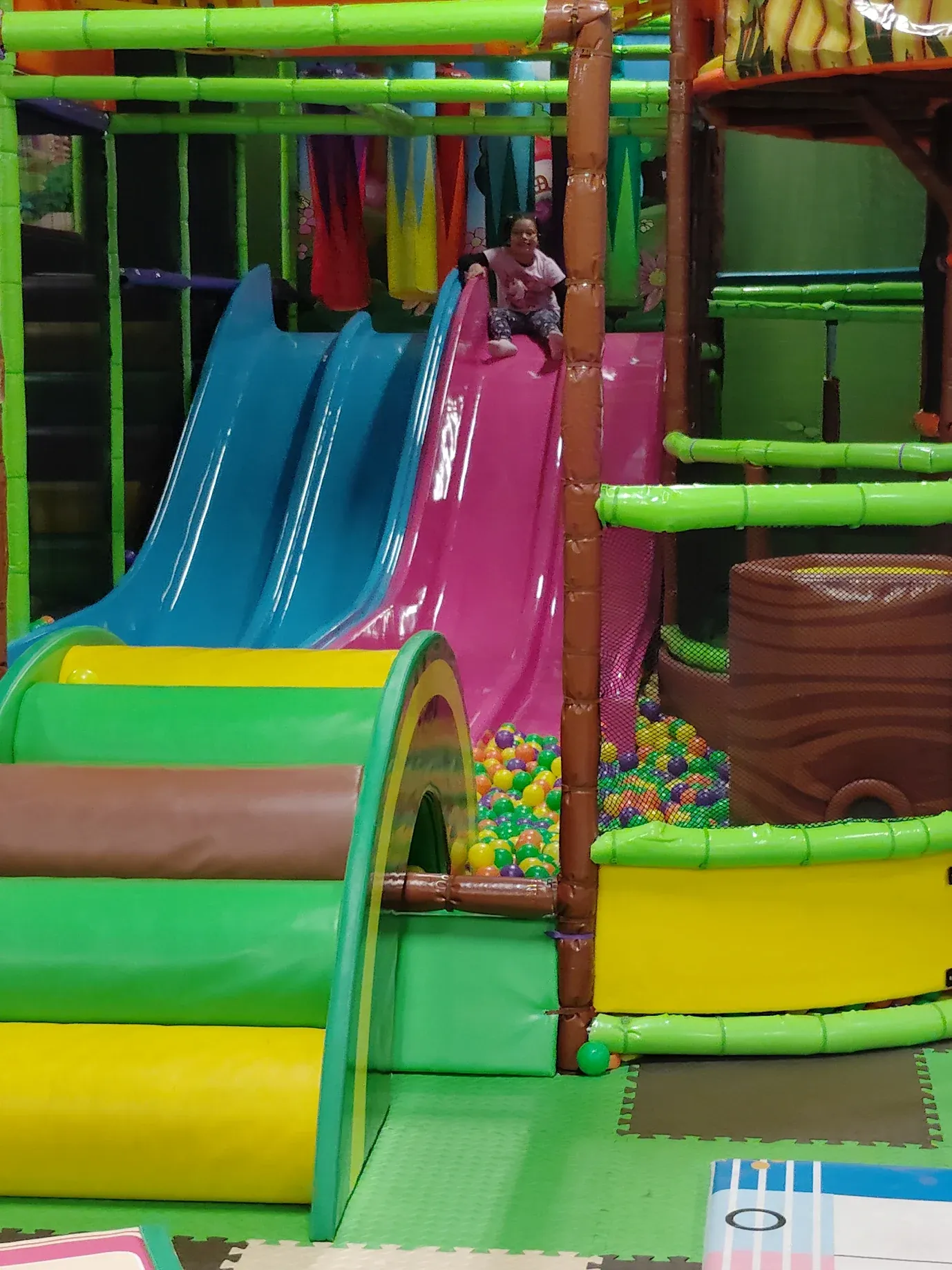 Child on pink slide in the indoor soft play area at SacTag.